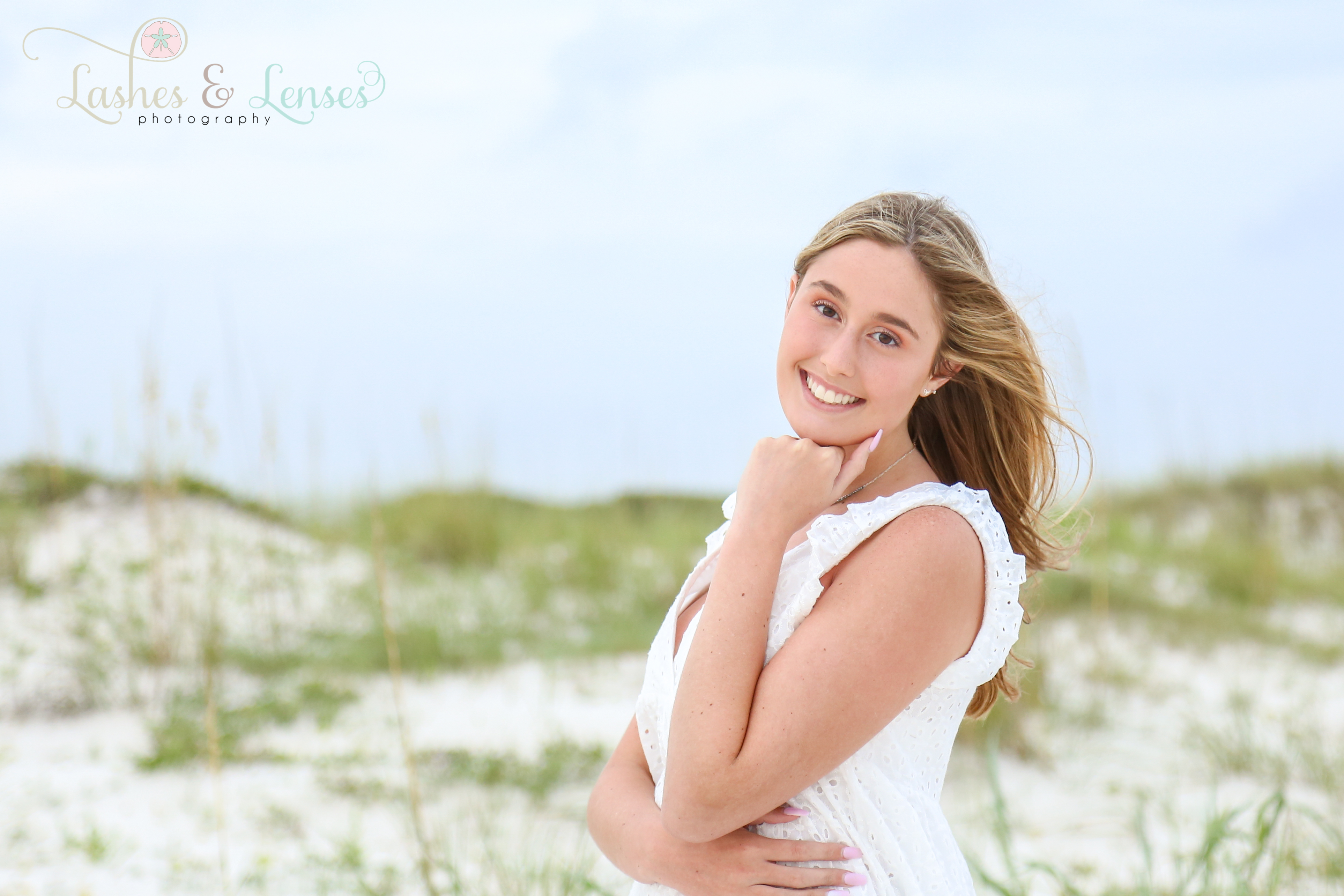 Blonde senior girl posing on the beach next to a sand dune at Johnsons Beach in Perdido Key