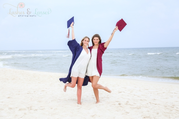 Two senior girls in their caps and gowns on the beach at Johnsons Beach in Perdido Key