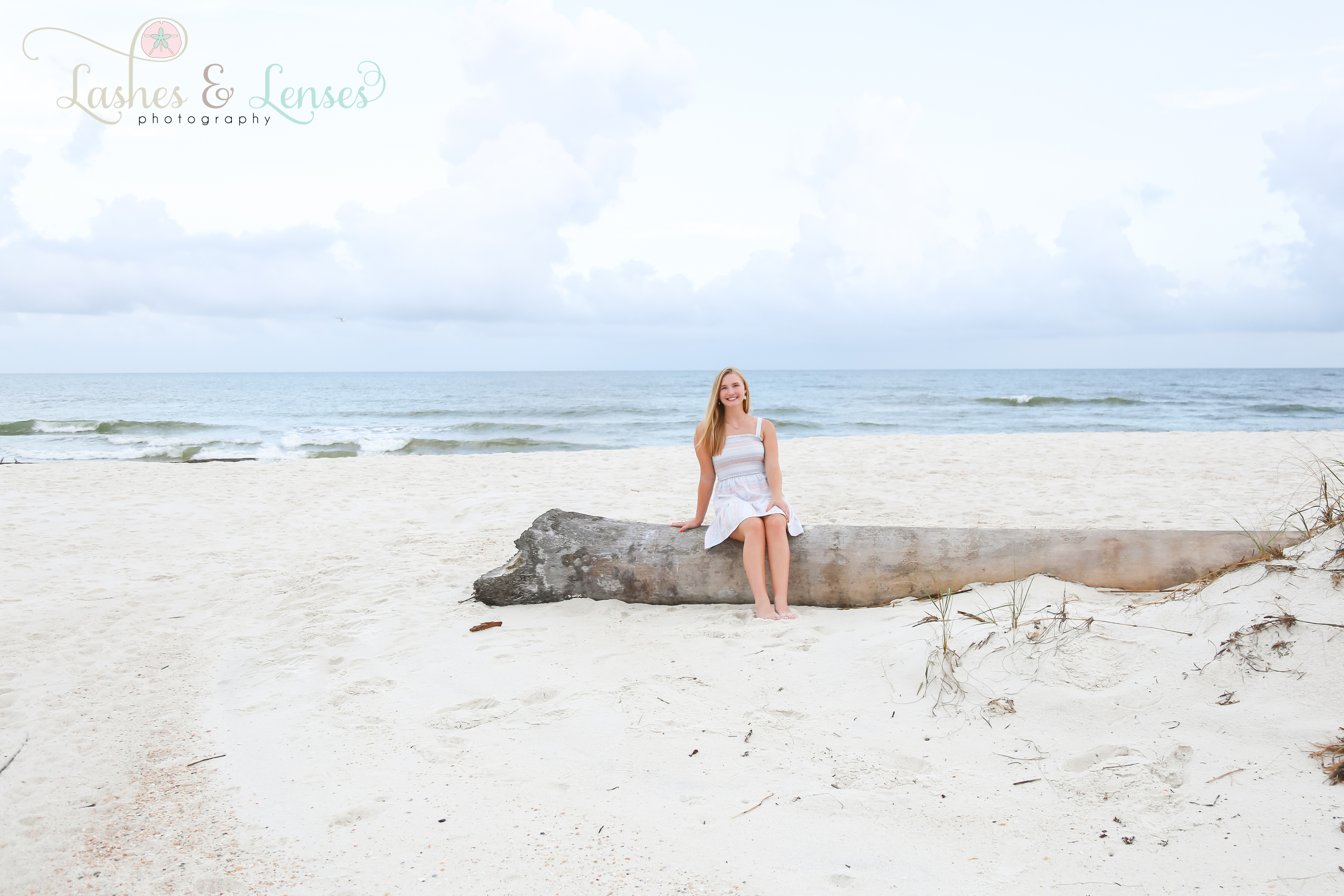 Senior Girl portrait sitting on a washed up tree at Johnson's Beach in Perdido Key