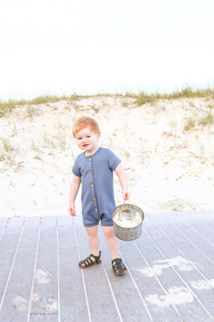 Toddler redheaded boy with bucket on the boardwalk at Johnsons Beach in Perdido Key Florida