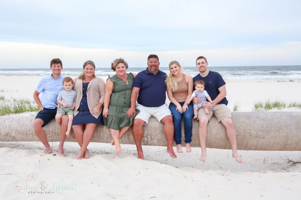 Extended family sitting on a washed up palm tree on the beach at Johnsons Beach in Perdido Key Florida