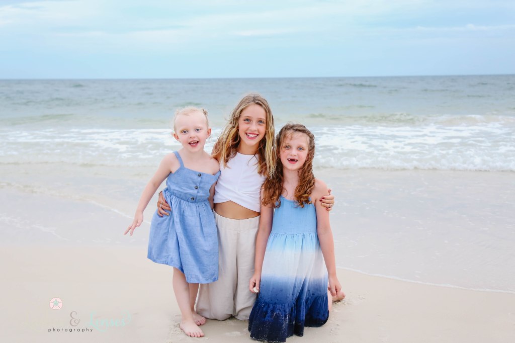 Three girl cousins kneeling and standing in front of the water at Johnsons Beach in Perdido Key Florida