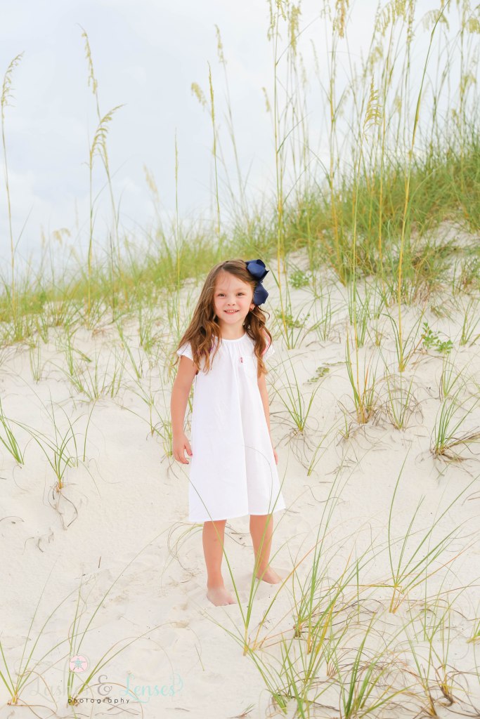 Preschool age girl standing in the sand with the sand dunes behind her and the sea oats at Johnsons Beach in Perdido Key Florida