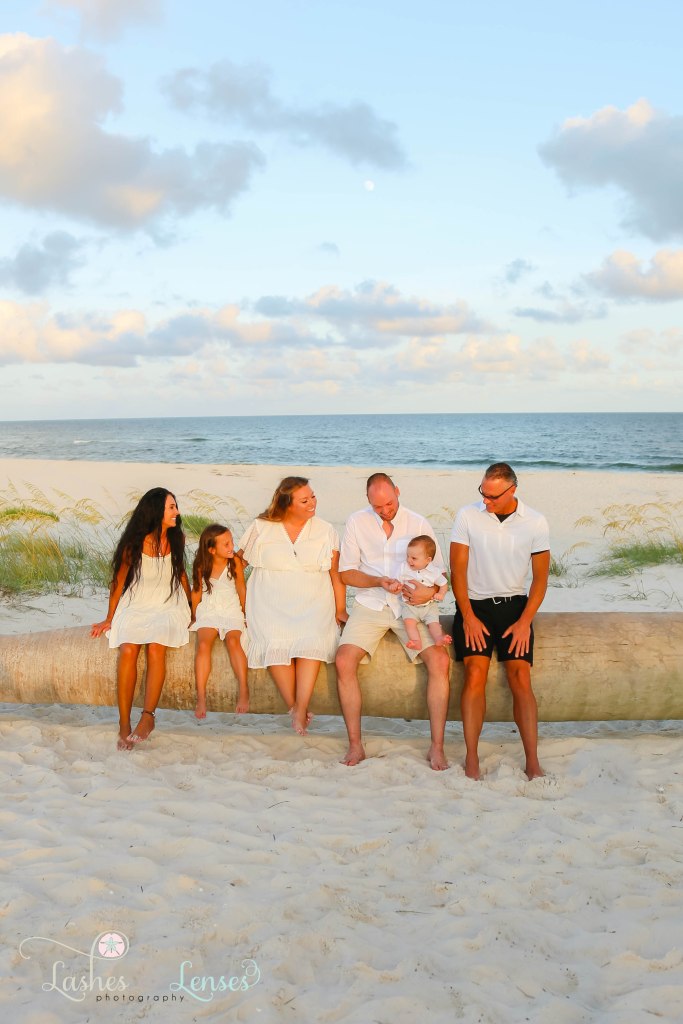 Family sitting on a washed up palm tree with the water behind them at Johnsons Beach in Perdido Key Florida