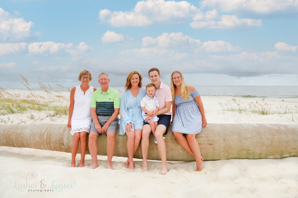 Extended family sitting on a washed up palm tree with the water behind them at Johnsons Beach in Perdido Key Florida