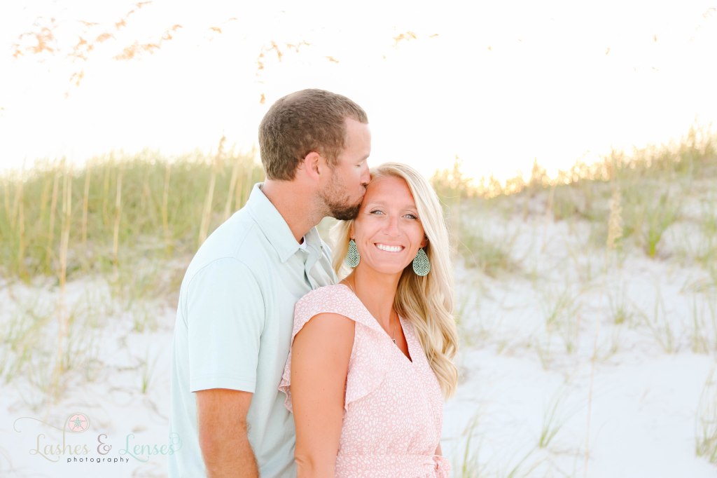 Husband kissing wife on the forehead with golden sea oats behind them at Johnsons Beach in Perdido Key Florida