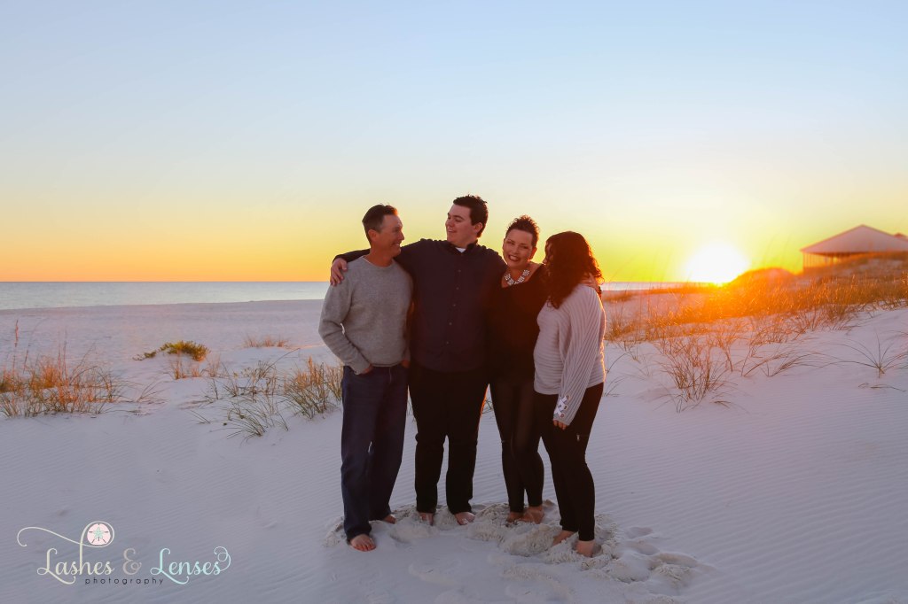 Mom and dad looking at their kids with the sun setting behind them at Johnsons Beach in Perdido Key, Fl