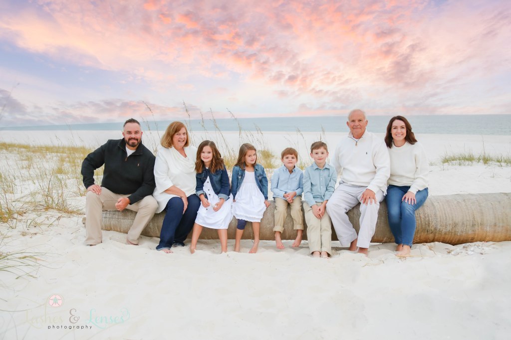 Extended family sitting on a washed up palm tree with a colorful sunset behind them at Johnsons Beach in Perdido Key, Fl
