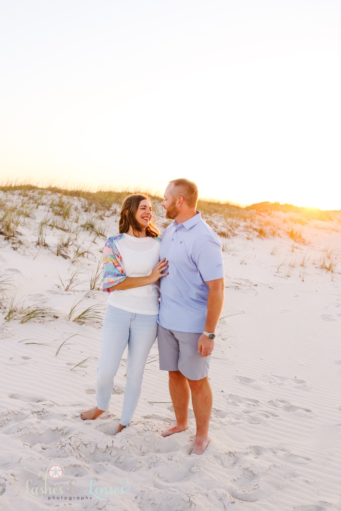 Husband and wife looking at each other with the golden sunset behind them and the sand dunes at Johnsons Beach in Perdido Key, Fl