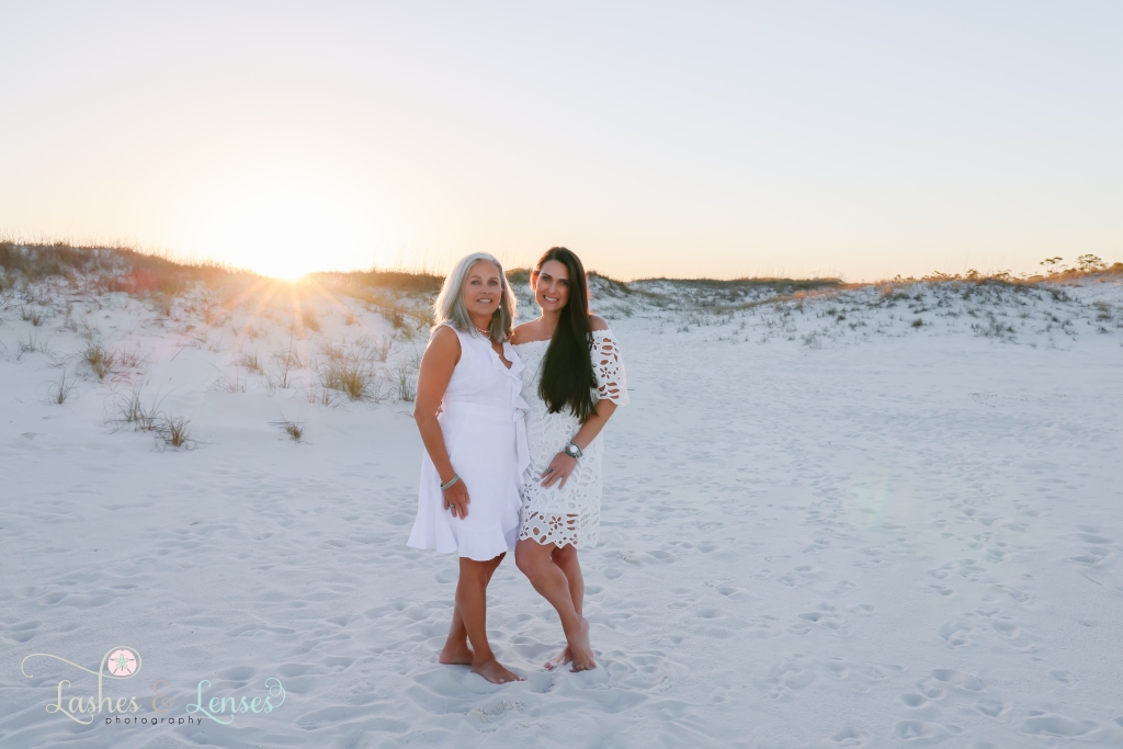 Mom and her adult daughter embracing with the sunset and sand dunes behind them at Johnsons Beach in Perdido Key, Fl