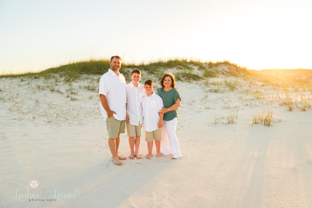 Family of four standing on the beach with the sunset and sand dunes behind them at Johnsons Beach in Perdido Key, Florida