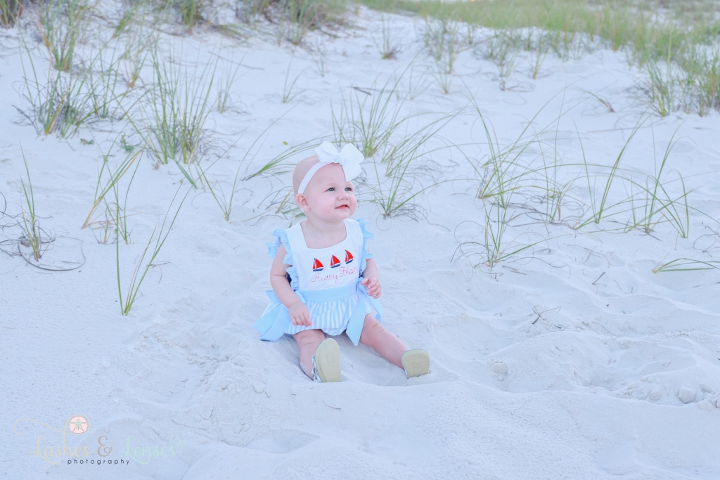 Baby girl sitting in the sand and looking off at her parents at Johnsons Beach in Perdido Key, Florida