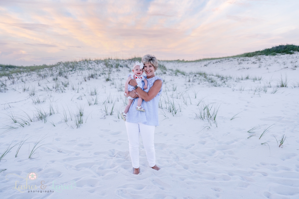 Grandma is holding and hugging her little granddaughter close with the sunset behind them at Johnsons Beach in Perdido Key, Florida