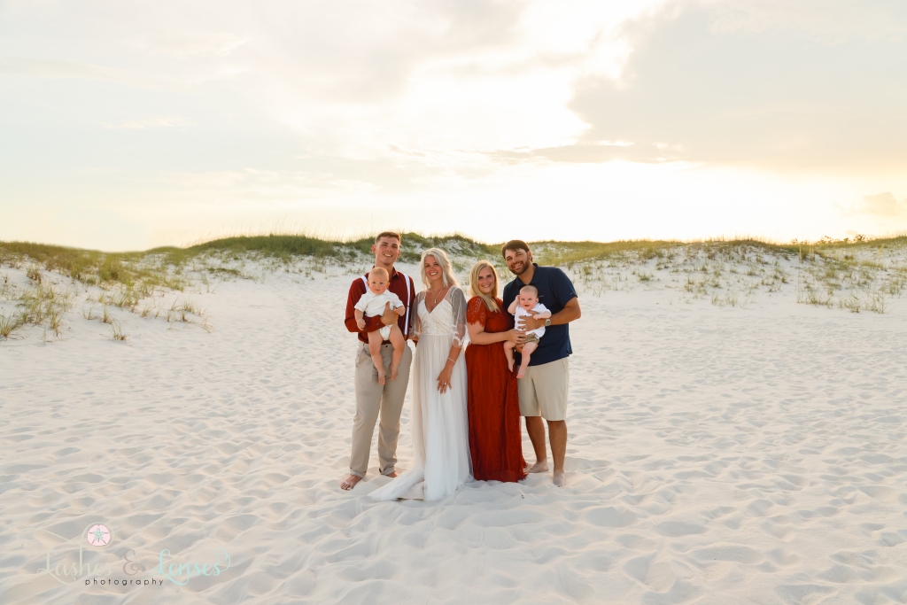 Bride and Groom holding their son and their best man and maid of honor holding their son with the sunset behind them at Johnsons Beach in Perdido Key, Florida