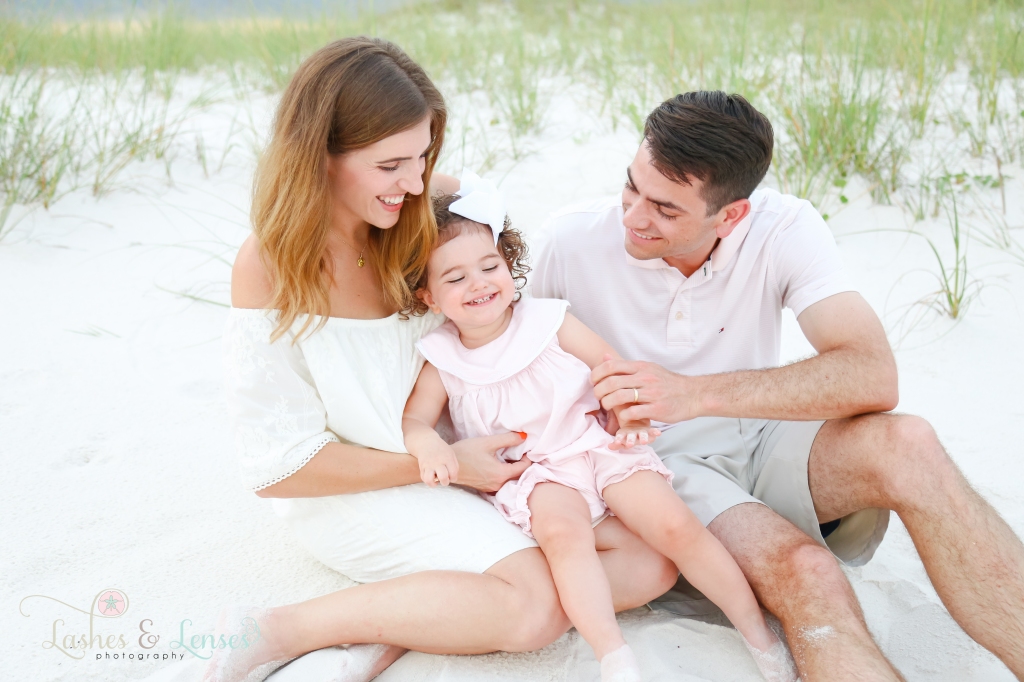 Mom and Dad sitting in the sand tickling their toddler daughter at Johnsons Beach in Perdido Key, Florida