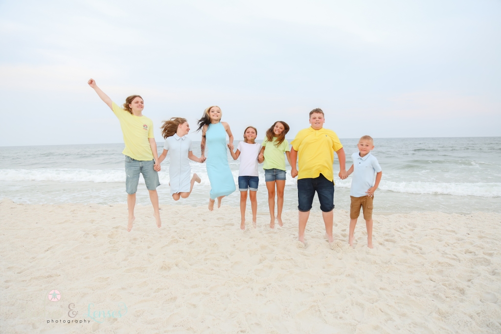 Seven cousins all jumping in the air at the edge of the water at Johnsons Beach in Perdido Key, Florida