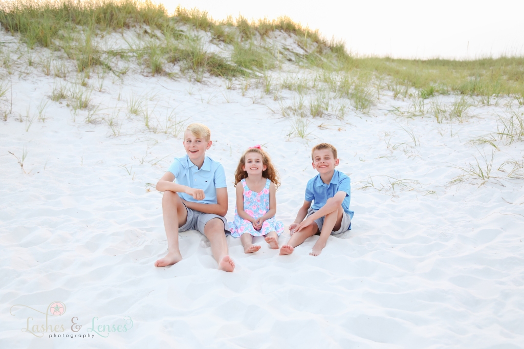 Two brothers and sister sitting in the sand with large sand dunes behind them at Johnsons Beach in Perdido Key, Florida