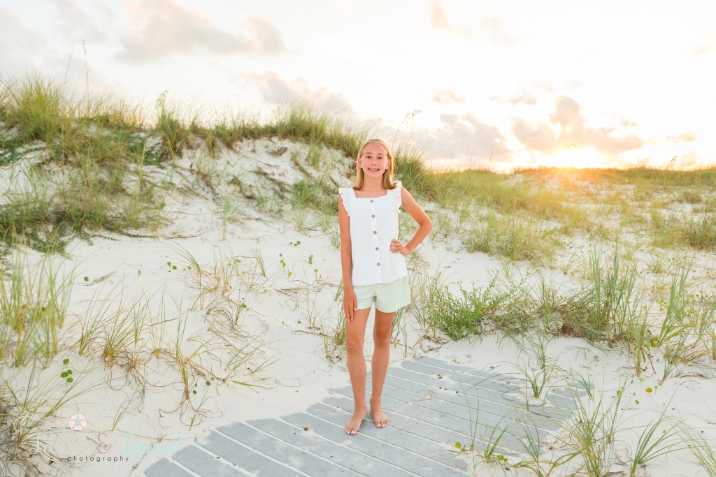Pre-teen girl standing on a washed up boardwalk with large sand dunes behind her at Johnsons Beach in Perdido Key, Florida