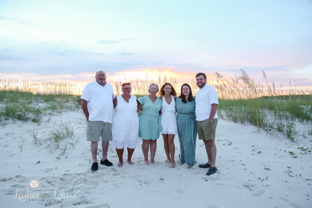 Extended family standing on the beach with sand dunes, sea oats and the sunset behind them at Johnsons Beach in Perdido Key, Florida