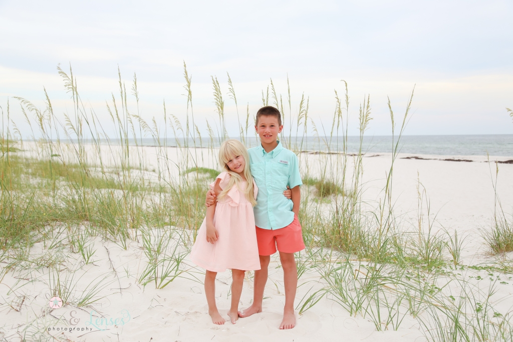Brother and Sister with their hands around each others waist with sea oats and the water behind them at Johnsons Beach in Perdido Key, Florida