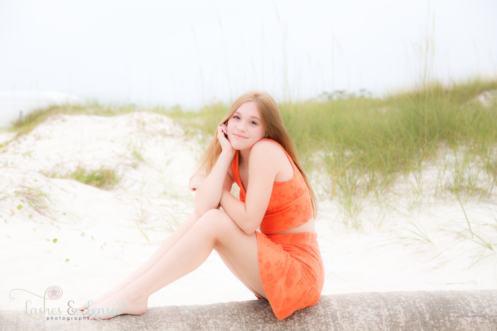 Teen girl sitting on a washed up palm tree at Johnsons Beach in Perdido Key, Florida