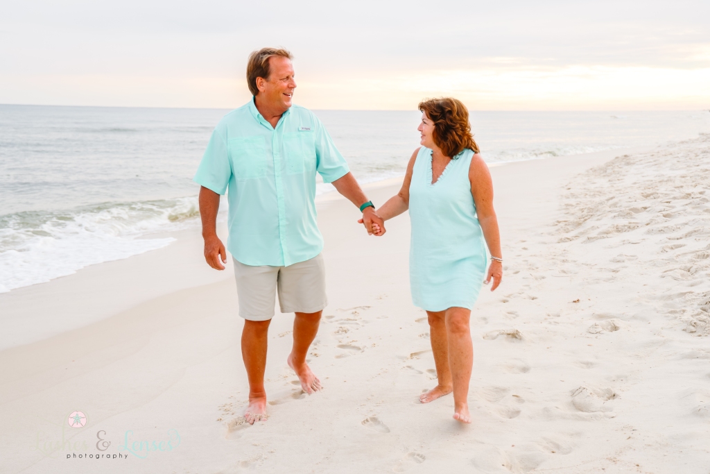 Husband and wife holding hands and walking along the edge of the water at Johnson's Beach in Perdido Key, Florida