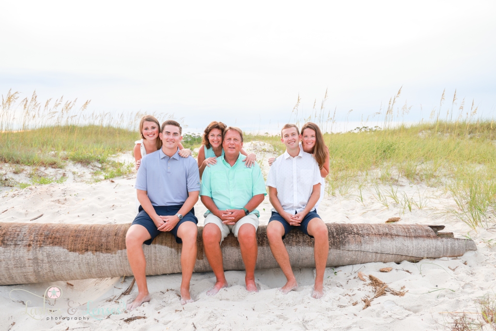 Three sets of couples, the men are sitting on a washed up palm tree with their wives standing behind them at Johnson's Beach in Perdido Key, Florida