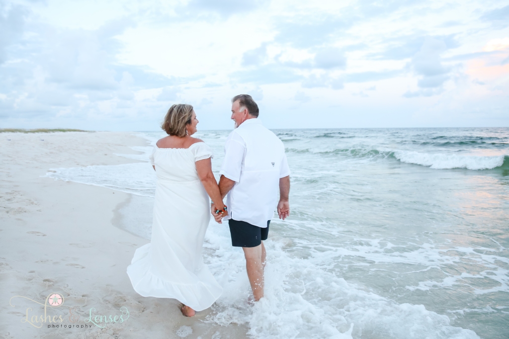 Husband and wife walking holding hands with their backs to the camera at Johnson's Beach in Perdido Key, Florida