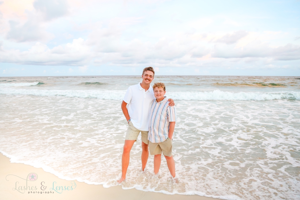 Two teen boy cousins standing in the water and smiling at the camera at Johnson's Beach in Perdido Key, Florida