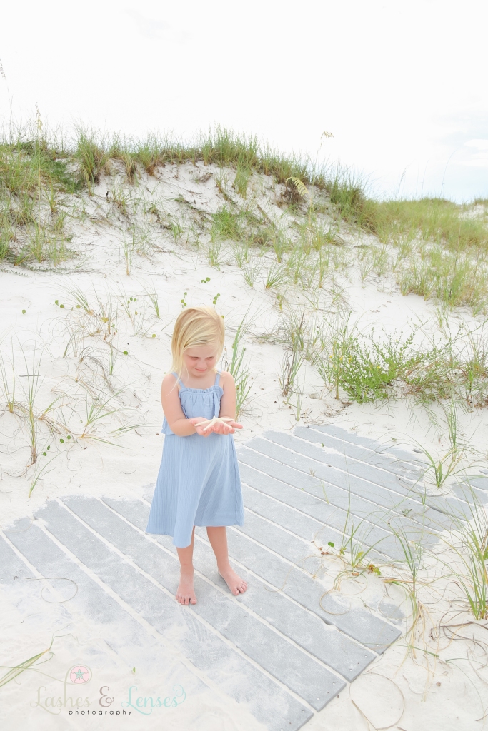 Toddler girl holding a starfish and looking at her hands at Johnson's Beach in Perdido Key, Florida