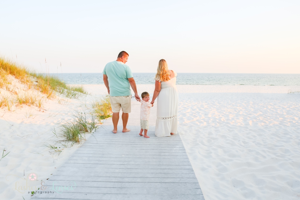 Mom and Dad walking down the boardwalk with their son turning around to look at the camera at Johnsons Beach in Perdido Key, Florida