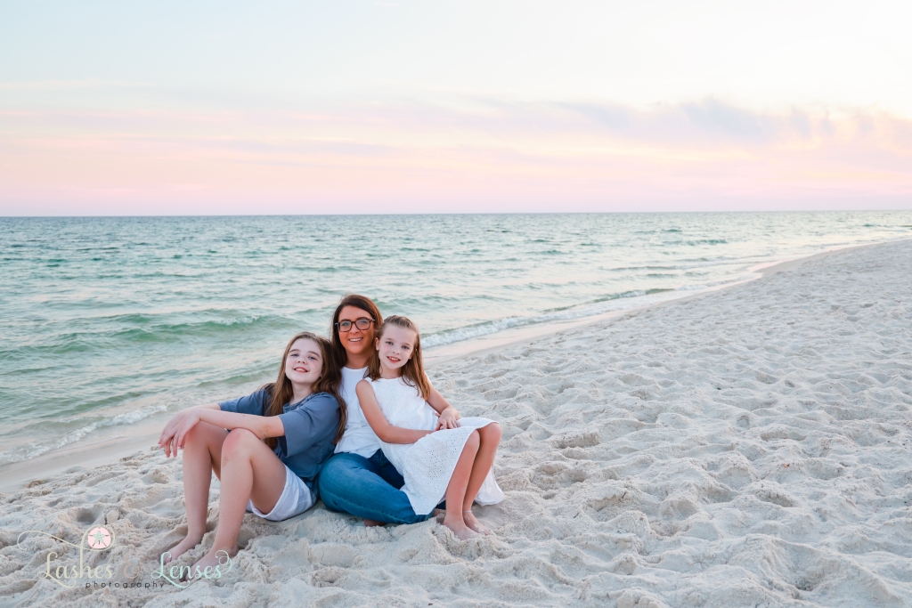 Aunt sitting in the sand with her nieces at the edge of the water at Johnsons Beach in Perdido Key, Florida