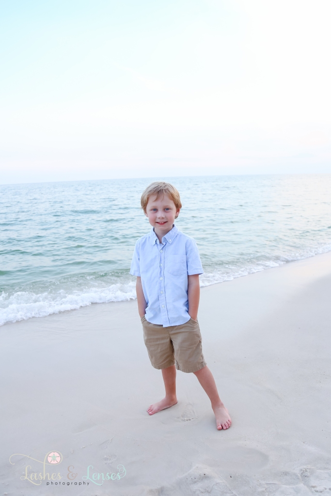 Young boy standing at the waters edge with his hands in his pockets at Johnsons Beach in Perdido Key, Florida