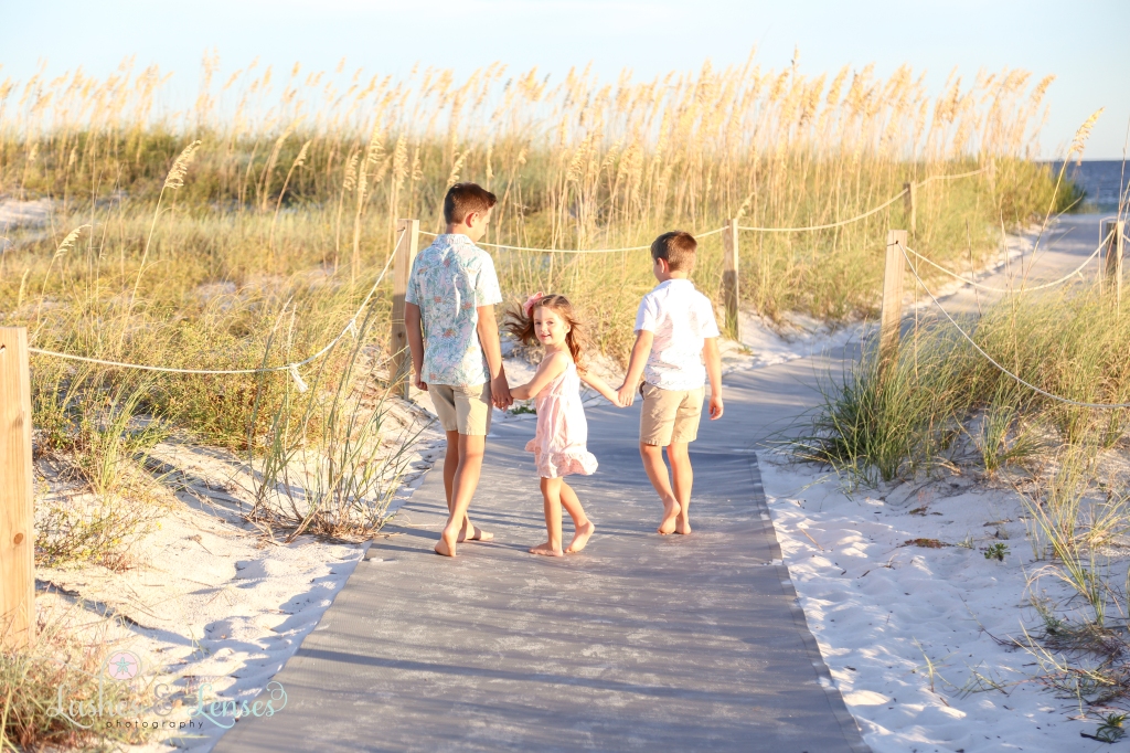 Two brothers and their young sister walking down the boardwalk towards the water with the little girl turning around to look at the camera at Perdido Key State Park in Perdido Key, Florida