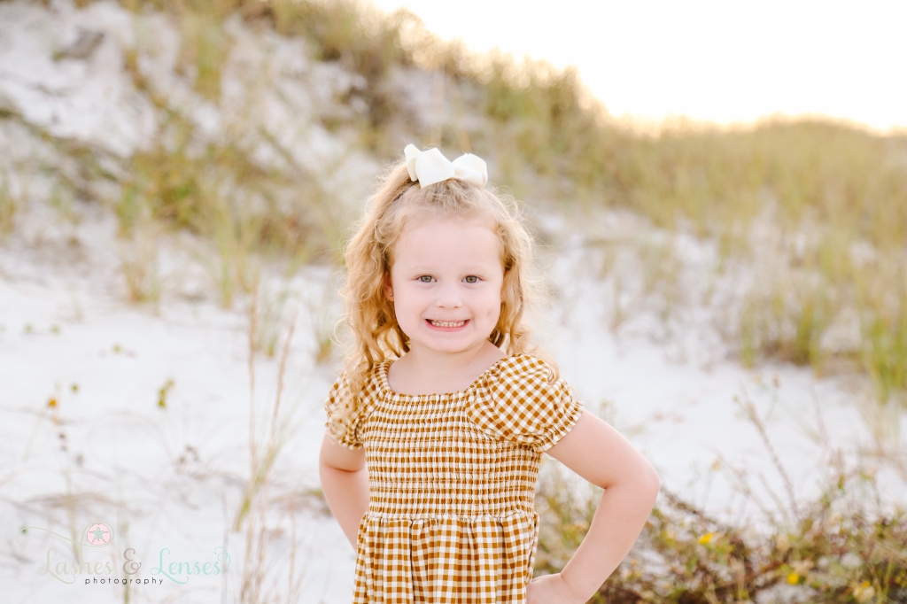 Close up photo of toddler girl with sand dunes behind her at Johnsons Beach in Perdido Key, FL