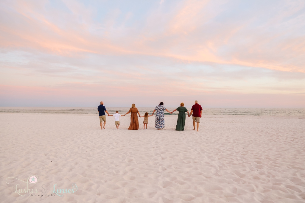 Extended family holding hands and walking down the beach towards the water at Johnsons Beach in Perdido Key, FL