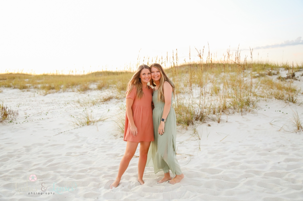 Sisters standing on the beach with large sand dunes and sea oats behind them at Johnsons Beach in Perdido Key, FL