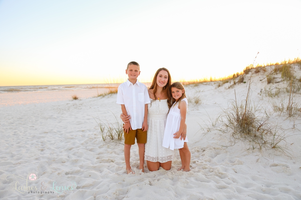 Mom kneeling in the sand with her son and daughter standing next to her at Johnsons Beach in Perdido Key, FL